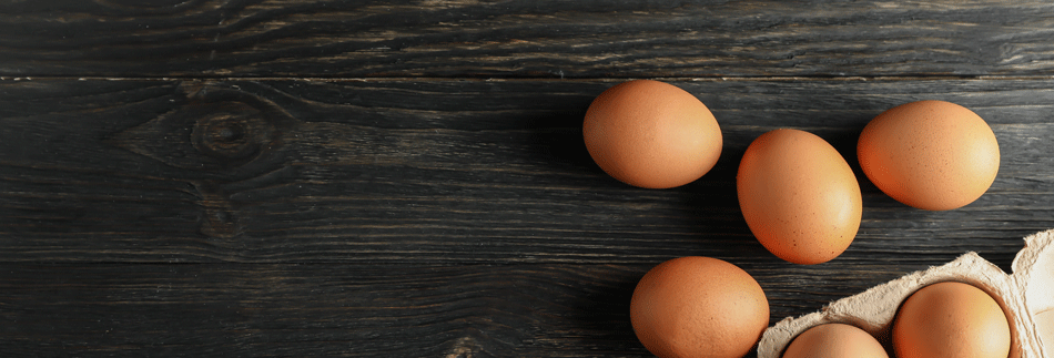 Vier Eier liegen auf einem dunklen Hintergrund, zwei Eier sind noch im Eierkarton. Beitrag Ostern